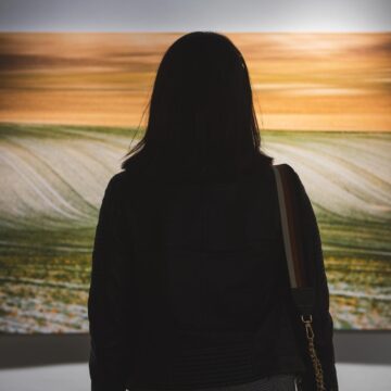 10 Famous Landscape Paintings: Details Easily Missed A woman views a large painting of rolling fields beneath an orange sky in a gallery.