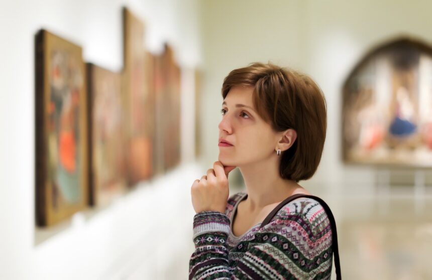 17 Famous Paintings of Women: Scandal, Theft and Fame A visitor studies a row of framed paintings in a softly lit art gallery.