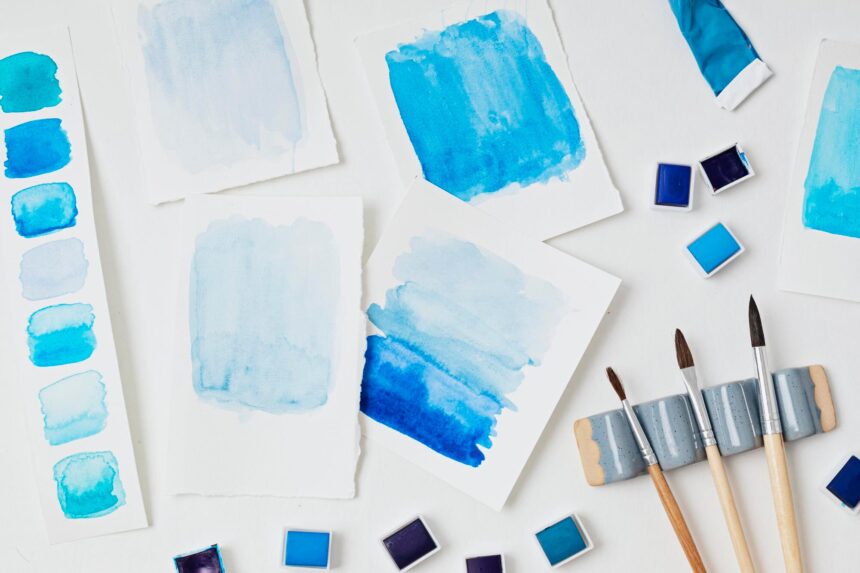 14 Famous Watercolor Paintings: Sharp Edges, Soft Washes Blue watercolor washes on sheets of paper beside paint pans and brushes on a white surface.