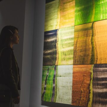 Why Famous Abstract Paintings Became Public Arguments A woman studies a large abstract painting with green, yellow, orange and dark rectangular blocks in a gallery.