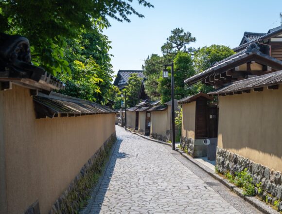 An empty stone-paved street lined with plaster walls and tiled roofs in Nagamachi, Kanazawa, Japan.