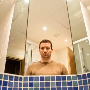 Bloody Mary Urban Legend: No Proven Link to the Queen A man's reflection in a bathroom mirror above a row of blue tiles.