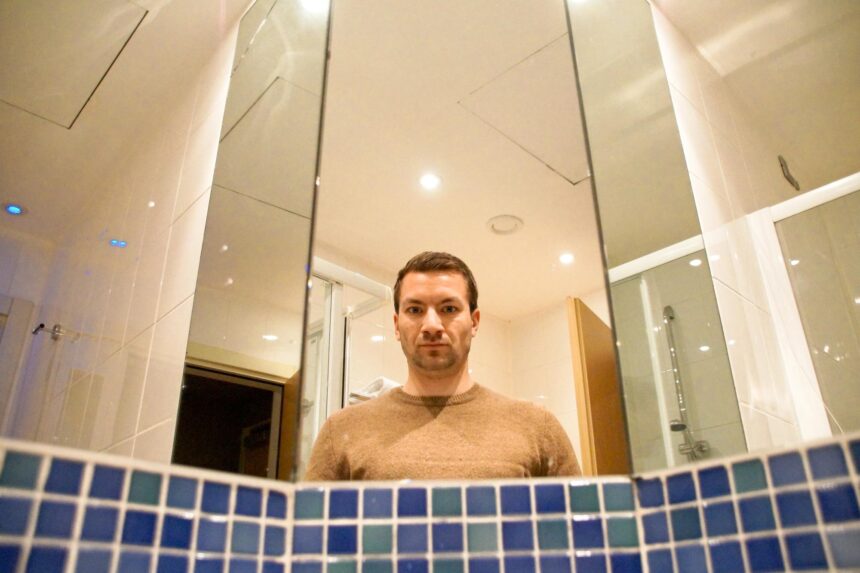Bloody Mary Urban Legend: No Proven Link to the Queen A man's reflection in a bathroom mirror above a row of blue tiles.