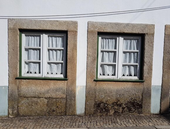 Tartarian Empire: Real Maps Behind a Lost-Empire Myth Two curtained windows with stone surrounds sit low above a cobbled pavement on a weathered facade.