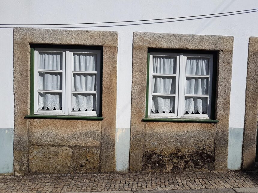 Tartarian Empire: Real Maps Behind a Lost-Empire Myth Two curtained windows with stone surrounds sit low above a cobbled pavement on a weathered facade.