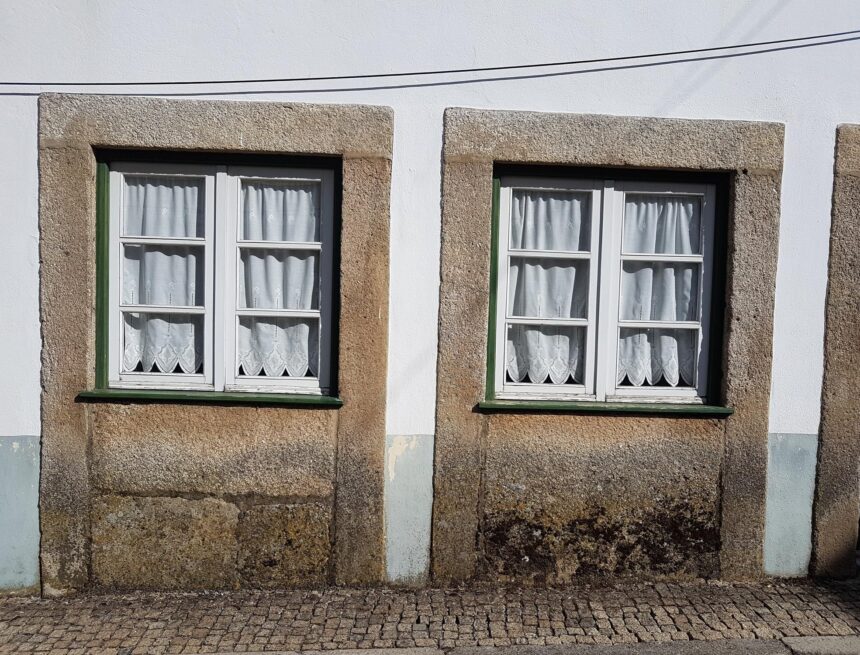 Tartarian Empire: Real Maps Behind a Lost-Empire Myth Two curtained windows with stone surrounds sit low above a cobbled pavement on a weathered facade.